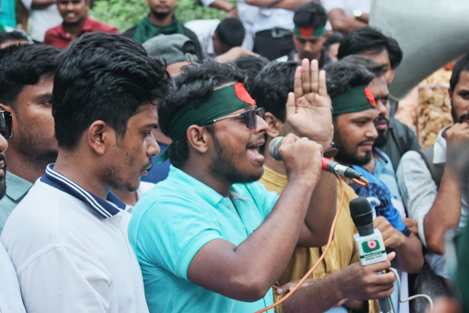 পতাকার ব্যান্ড পরে মাইকে স্লোগান দিচ্ছেন নাজমুল হাসান, পাশে নেতাকর্মীরা